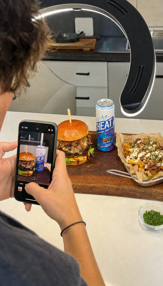 A food creator filming an overhead of a loaded burger with a phone, kitchen, ring light
