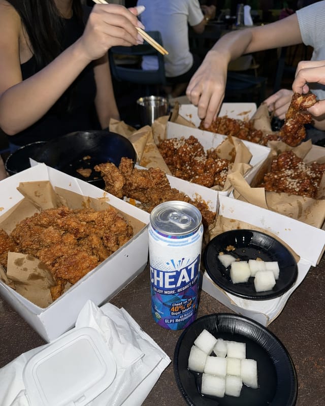 Korean fried chicken spread on a table in a busy late-night restaurant, pickled radish, wet wipes, friends' hands reaching in, harsh flash