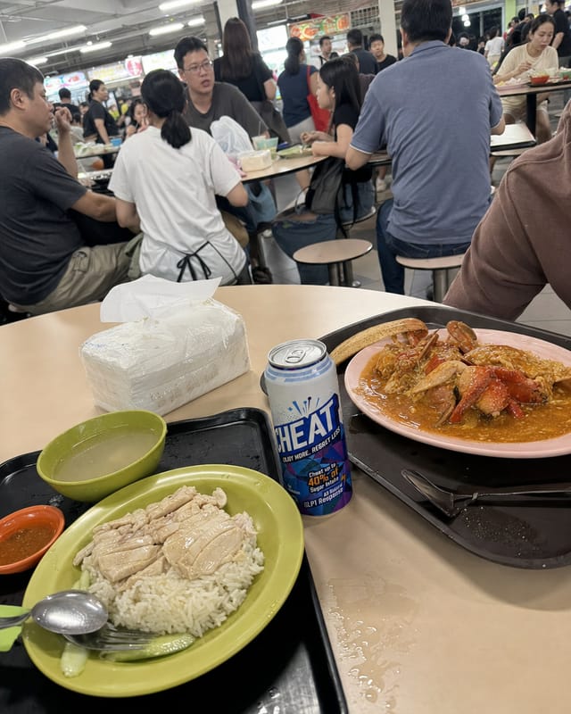 Singapore hawker centre table with chicken rice and chili crab, tissue packets, plastic trays, fluorescent light, crowd