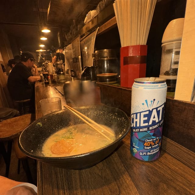 Late-night ramen counter in Tokyo, a half-eaten bowl of tonkotsu ramen, chopsticks resting on the bowl, steam, small wooden counter, warm la