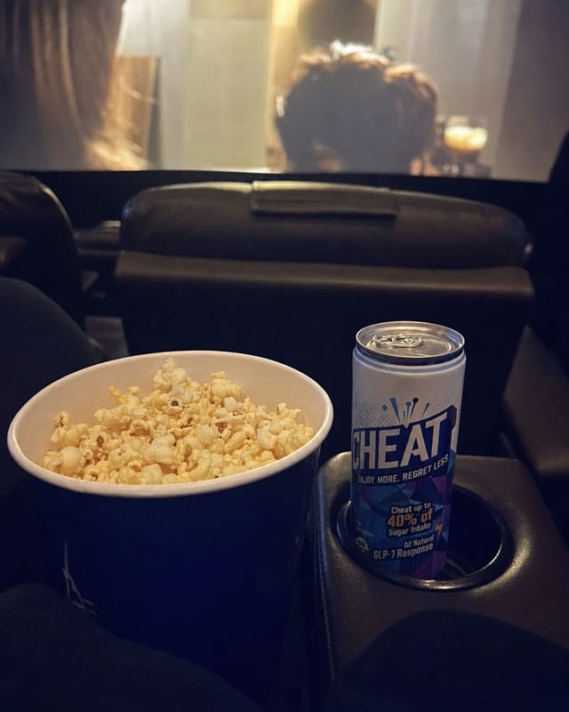 Cinema seat with a large popcorn bucket, screen glow, dark, phone photo