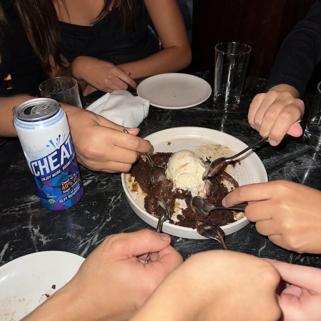A shared dessert table: molten chocolate cake, ice cream, spoons from multiple people, flash