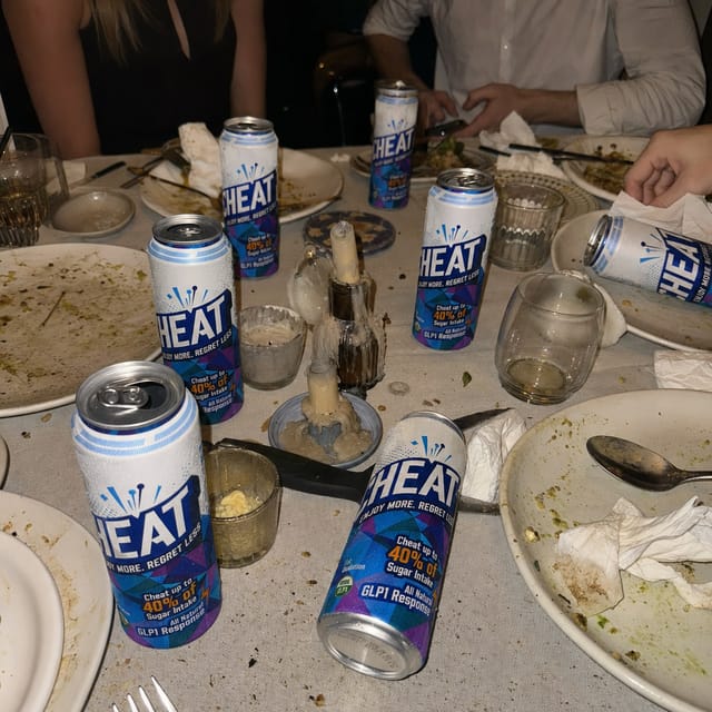 The end of a dinner party: a messy table with empty plates, crumbs, napkins, candles burned down, several empty aluminium cans